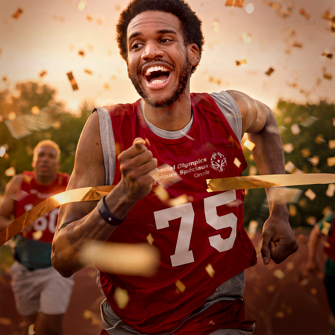 Man in a red special olympics shirt running while gold confetti falls around him 