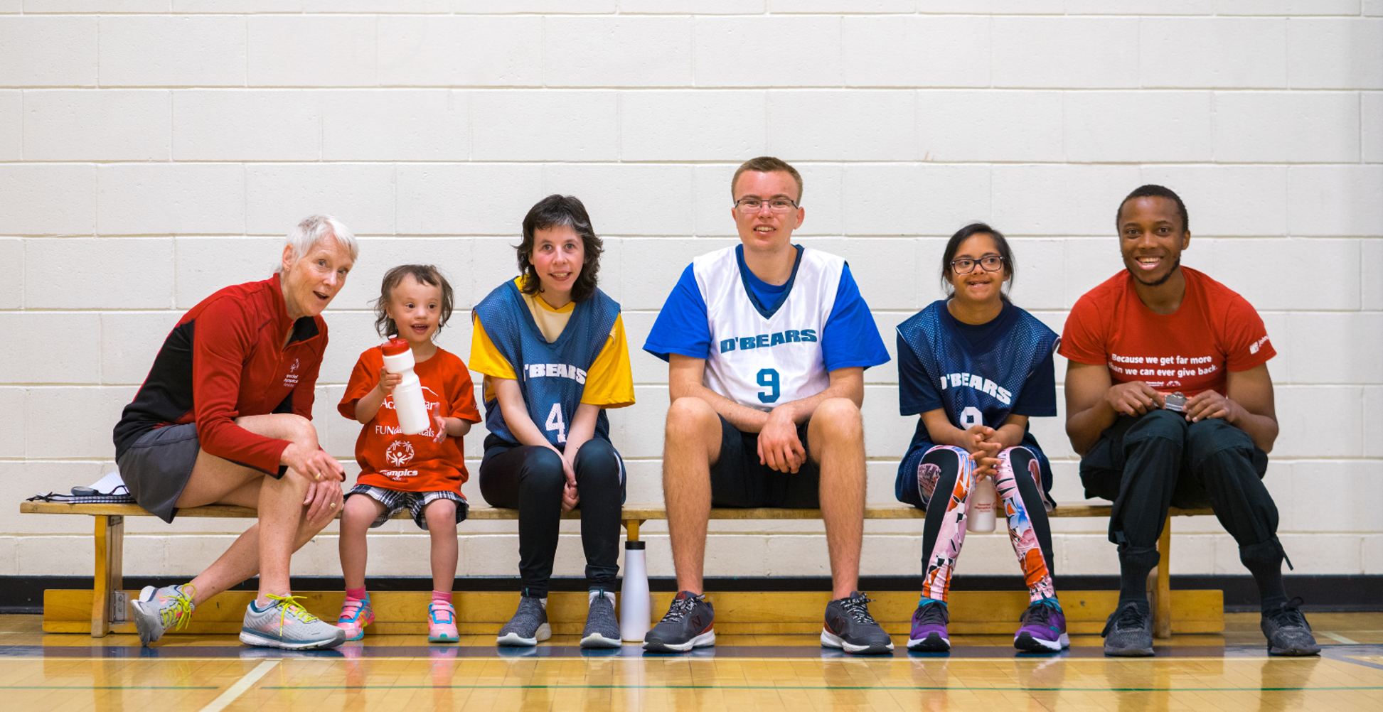Diverse group of people sitting on a bench smiling at the camera. 